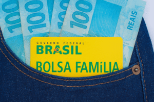 Cartão do Bolsa Família no bolso de jeans com notas de 100 reais.